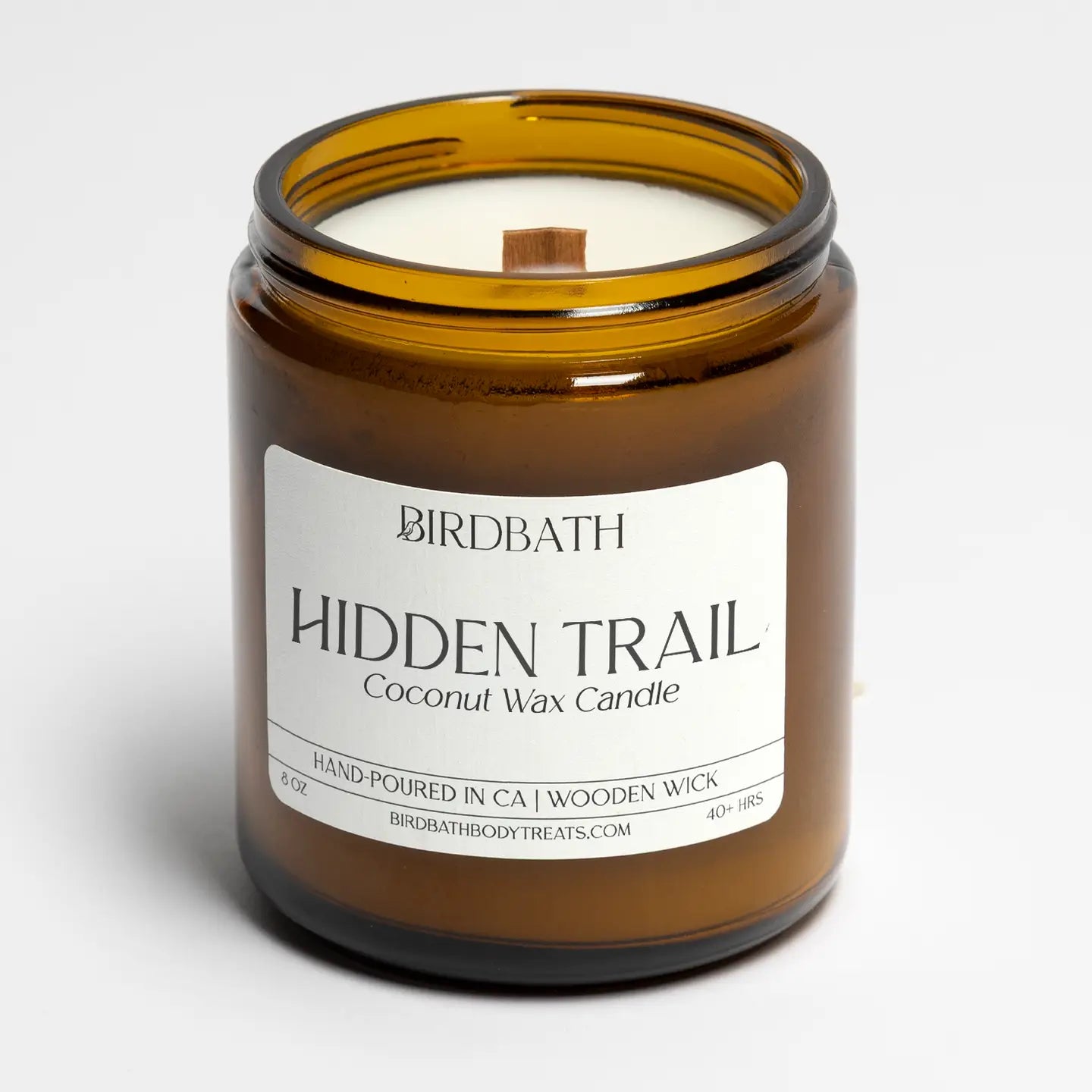 A Birdbath Hidden Trail coconut wax candle in an amber glass jar with a white label, set against a clean white background.