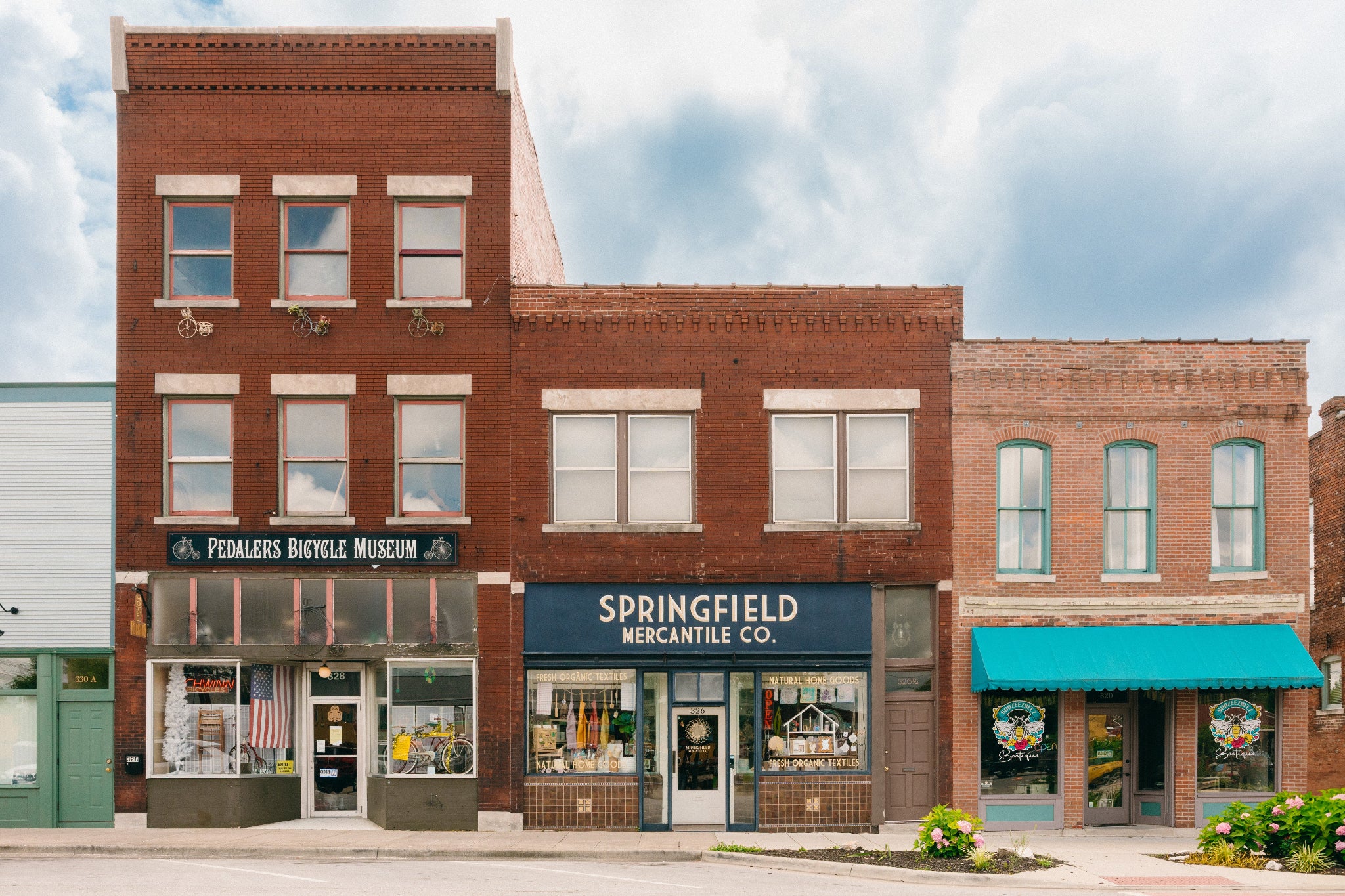 Brick building with storefronts including 'Springfield Mercantile Co.' and 'Peddlers Bicycle Museum' under a blue sky.

Description: Banner image of Springfield Mercantile Co. building storefront inviting customers to learn about us on the about page. 
Keywords: Springfield Mercantile Co., About Us, Historic Commercial St, building storefront image, online shop, Shopify
