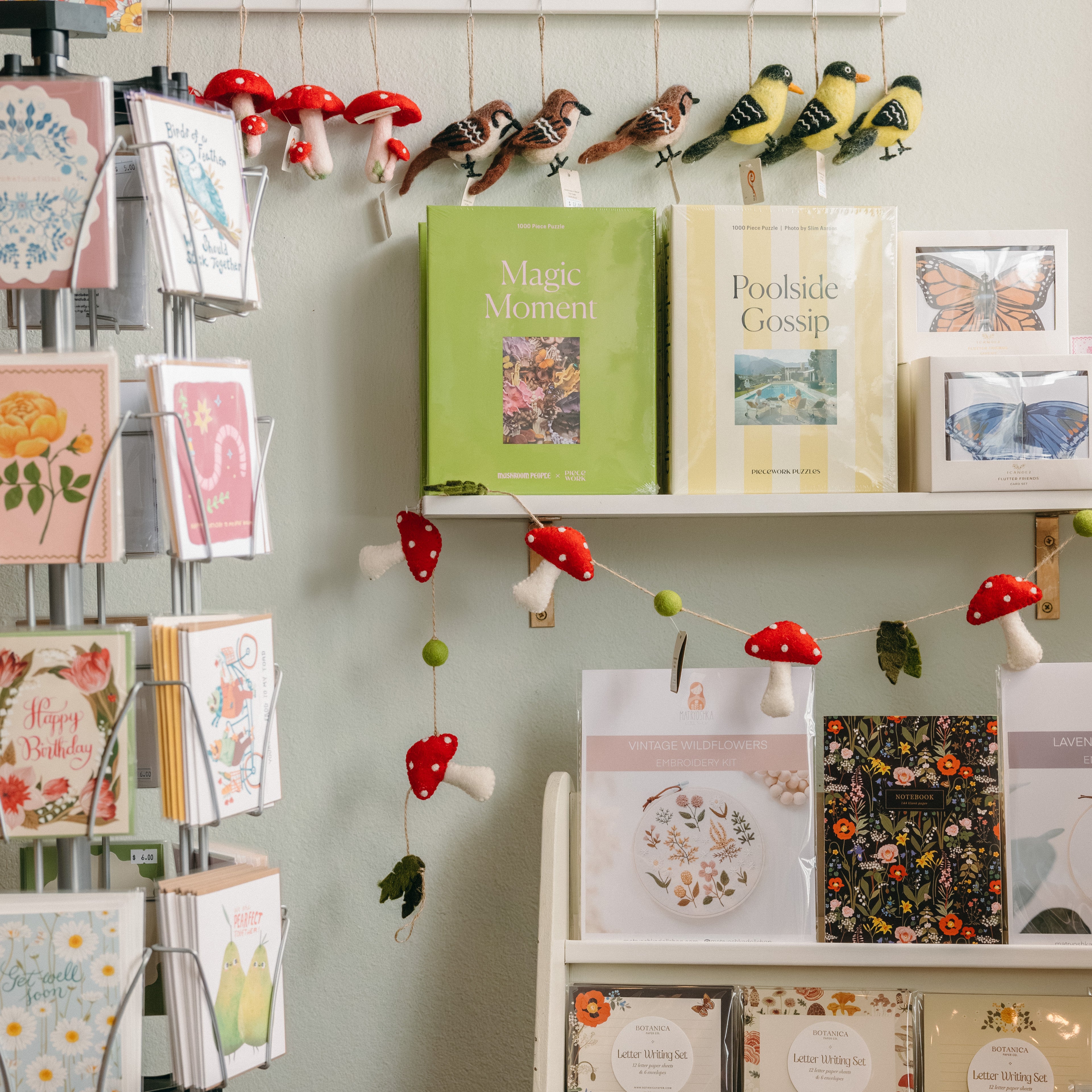 Display of greeting cards, art supplies and journals on shelves with a decorative mushroom garland.

Description: Categories image promoting Art Supplies, Cards & Journal goods on the Springfield Mercantile Co. homepage. 
Keywords: Springfield Mercantile Co., art supplies cards and journals, categories section, online boutique, Shopify