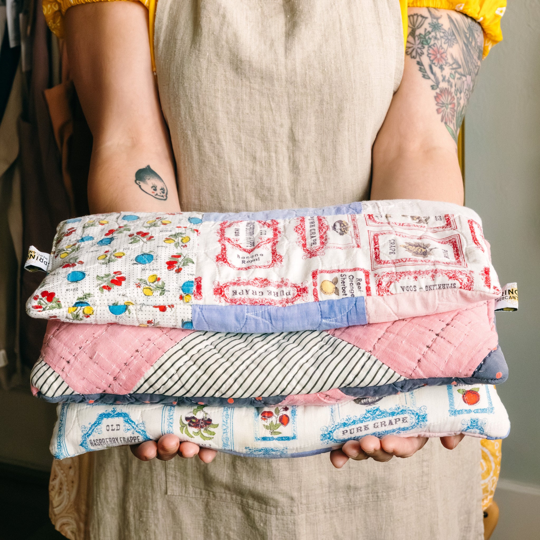 Person holding a stack of three handmade colorful rice bags with whimsical patterns made from antique quilts.

Description: Categories image promoting Handmade goods on the Springfield Mercantile Co. homepage. 
Keywords: Springfield Mercantile Co., handmade, categories section, online boutique, Shopify
