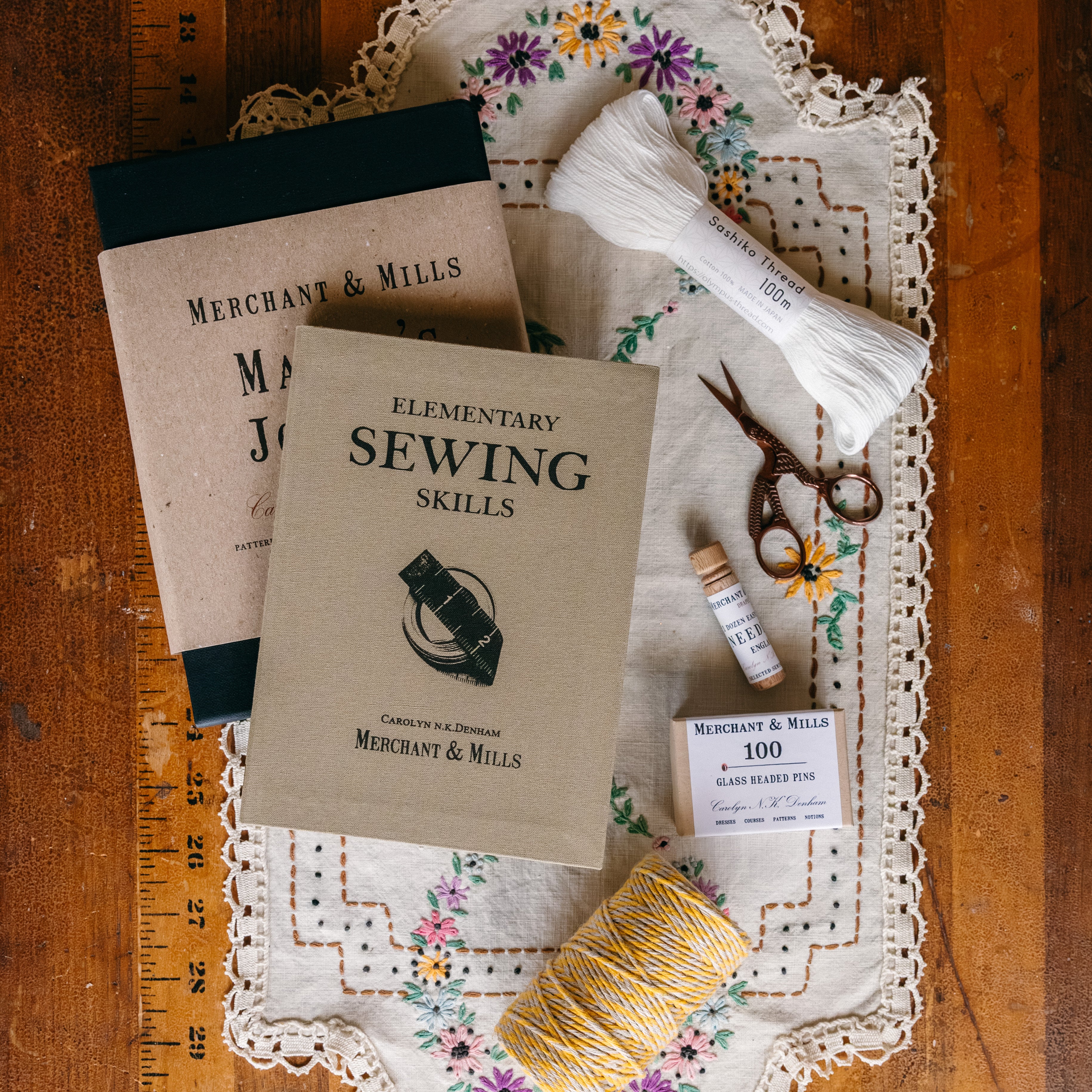 Sewing kits with needles, thread, and scissors resting on a doily placed on an antique wooden sewing table.

Description: Categories image promoting Sewing & Crafts goods on the Springfield Mercantile Co. homepage. 
Keywords: Springfield Mercantile Co., sewing and crafts, categories section, online store, Shopify