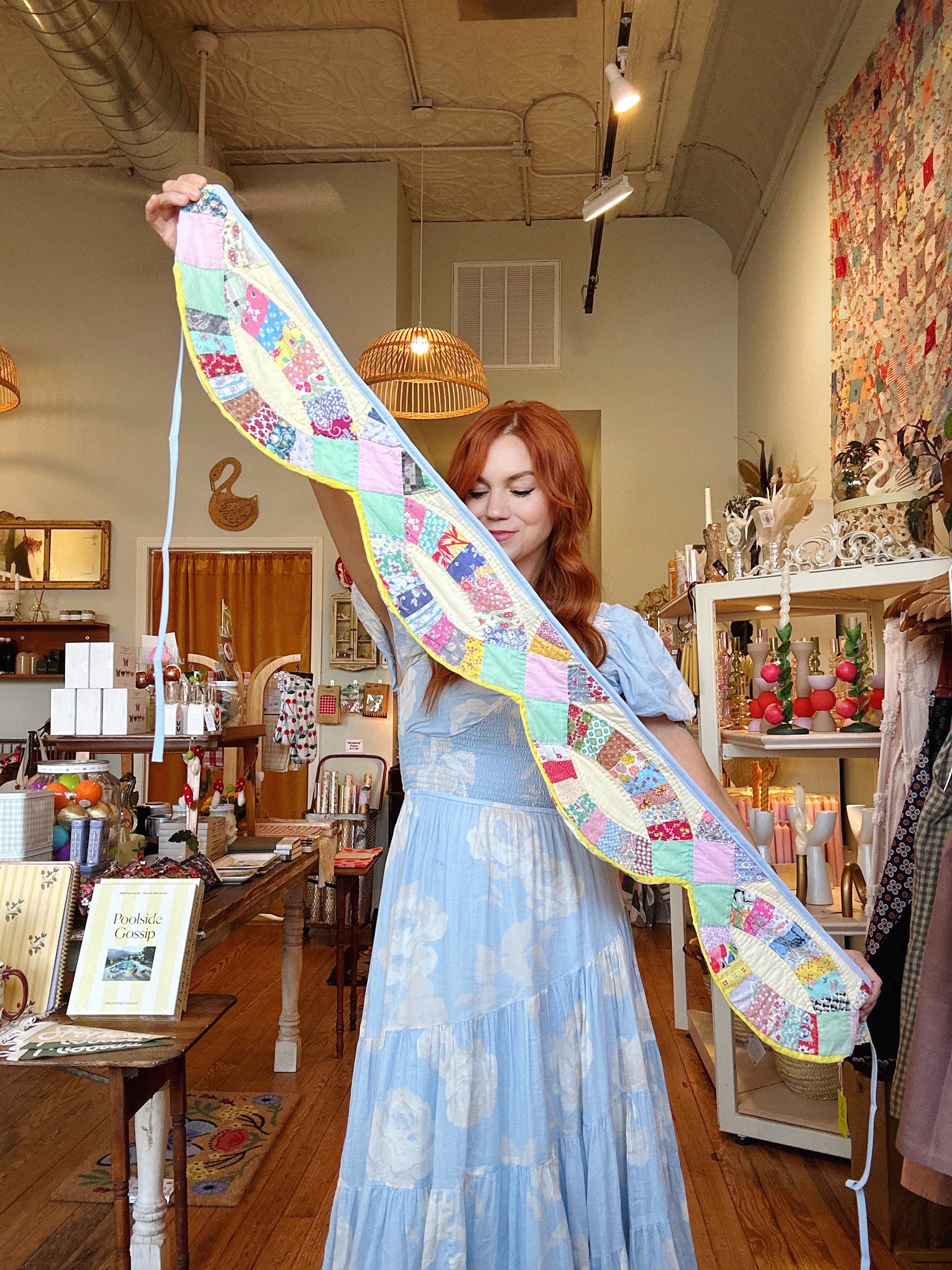 Woman holding a long, colorful quilt in a store setting